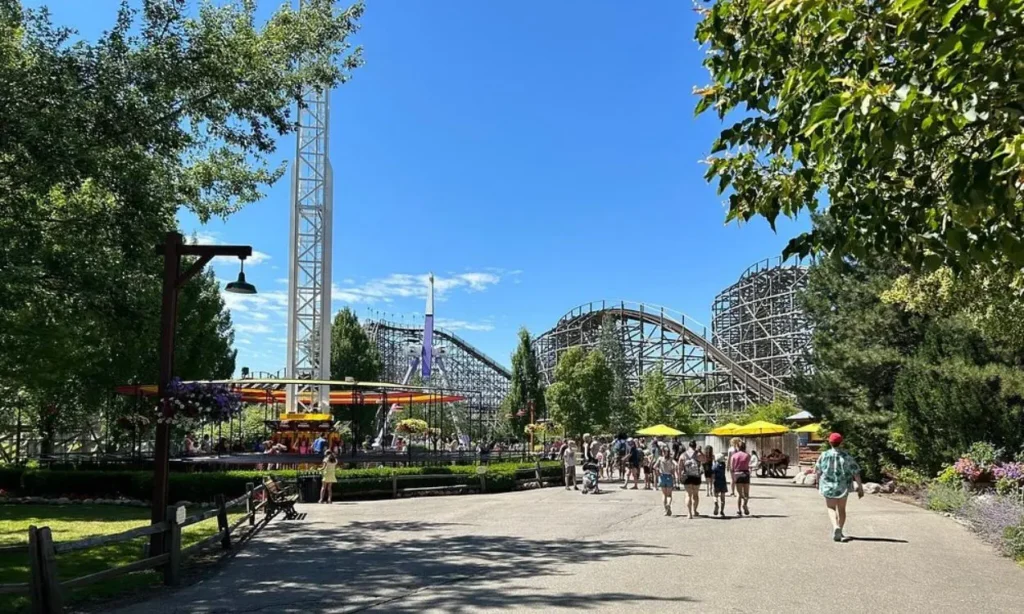 Visitors stroll through Silverwood Theme Park with rides and a wooden roller coaster in the background.