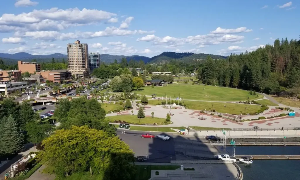 An aerial view of Downtown Coeur d'Alene with buildings, a park, and surrounding forested hills.