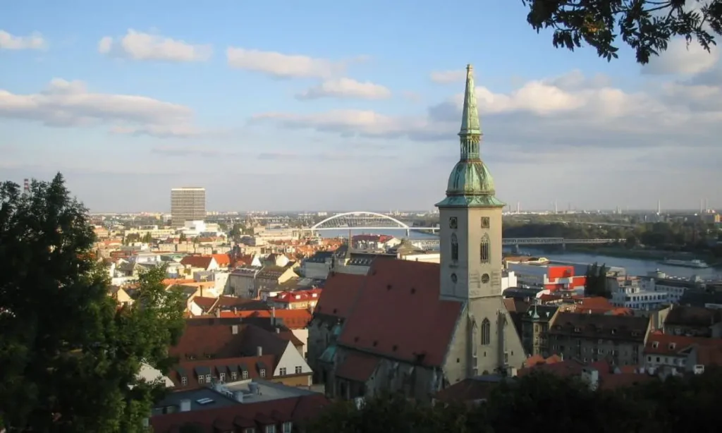 A cityscape of Slovakia with a church tower in the foreground and a bridge over the river.