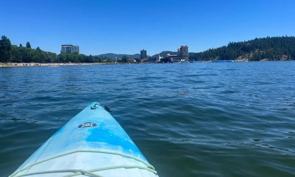 A kayak floats on the water with a clear view of Lake Coeur d'Alene and the city skyline ahead.