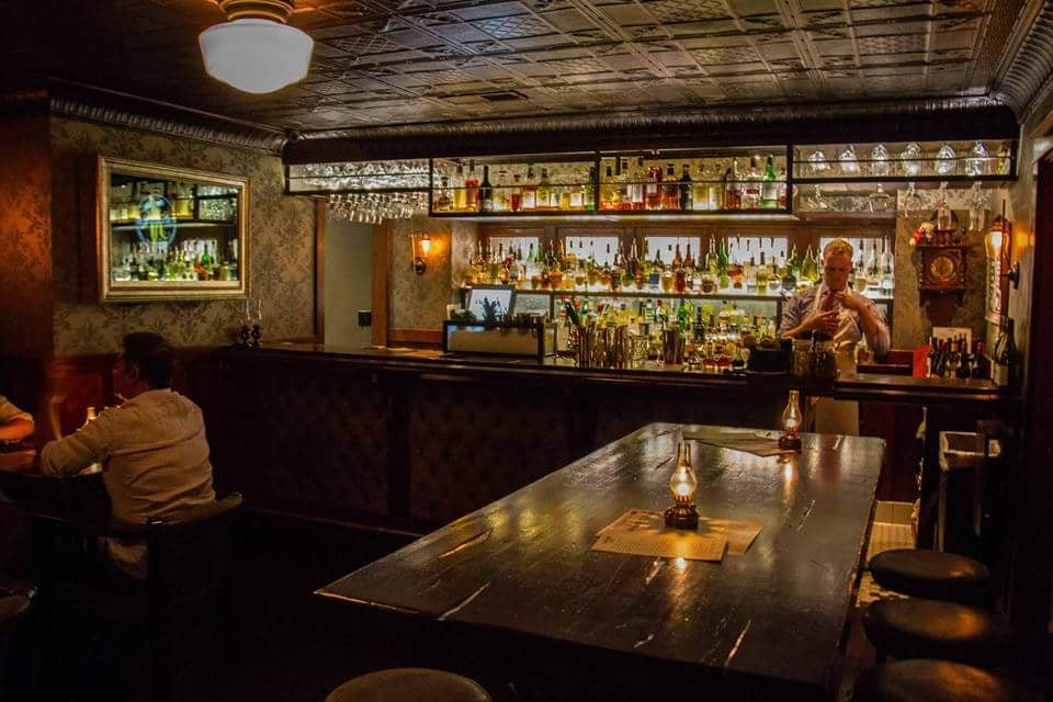 A dimly lit bar interior at The Raymond 1886 with a bartender preparing drinks.