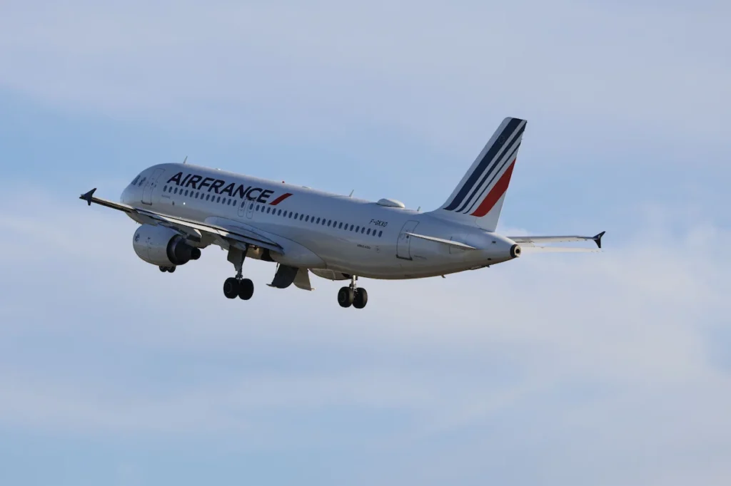 Air France Airbus A320 airplane with landing gear down against a hazy blue sky