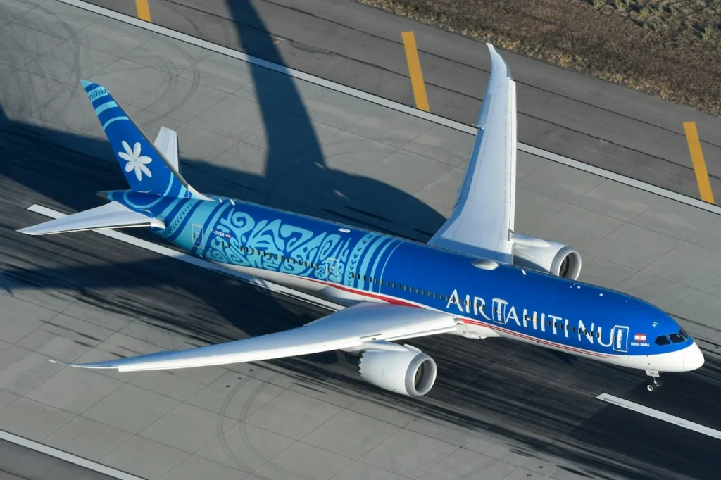 An overhead view of a blue and white Air Tahiti Nui Boeing 787-9 Dreamliner taxiing on the airport runway