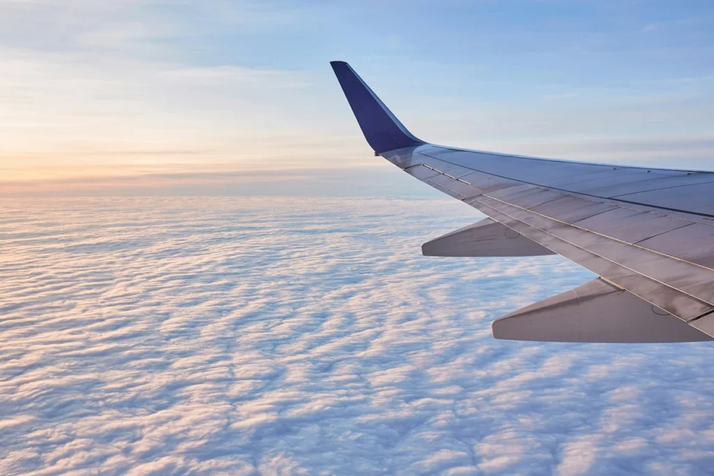 View of an airplane wing flying above a dense blanket of clouds during sunset