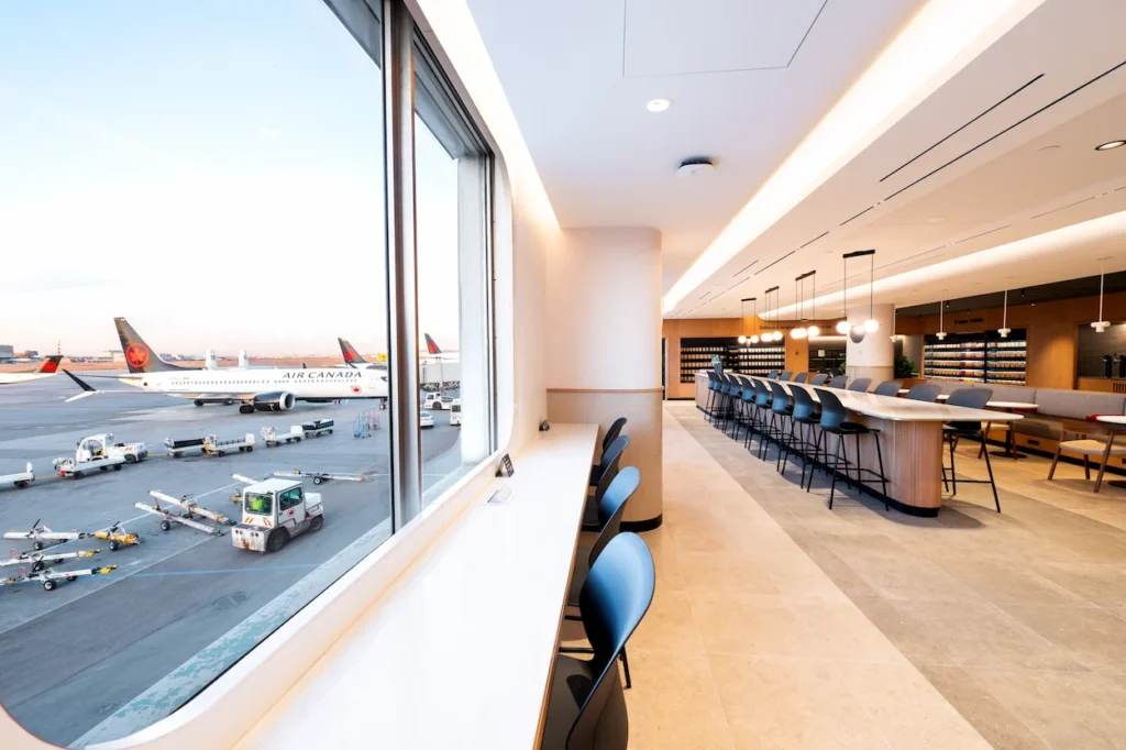 A modern airport lounge interior with counter seating looking out a window at airplanes
