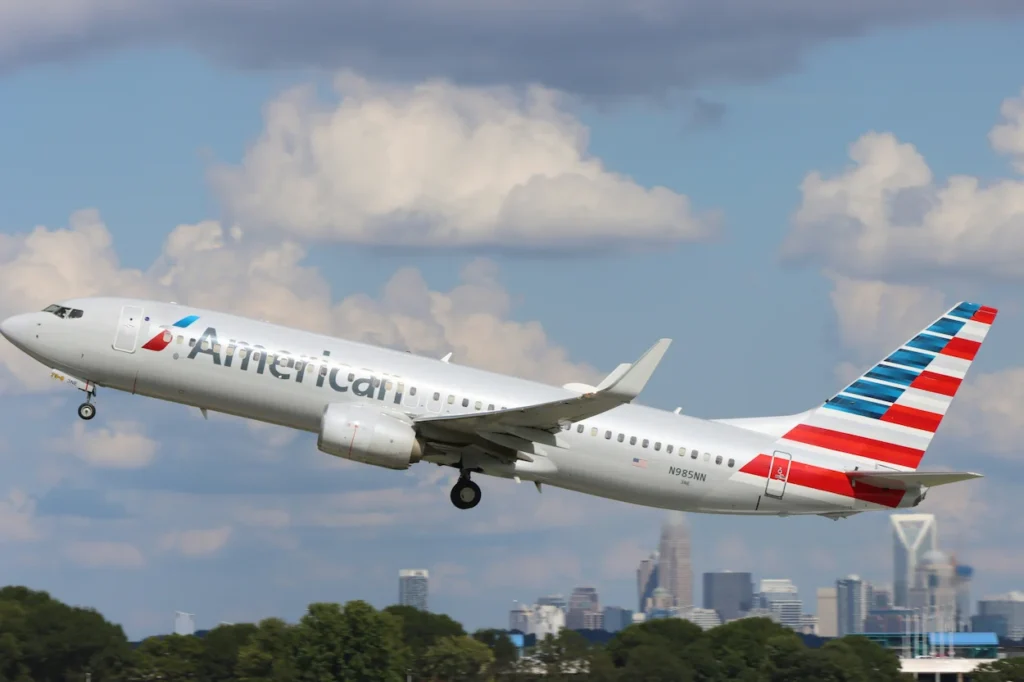 American Airlines Boeing 737-800 passenger airplane climbing into the sky during takeoff with a city skyline backdrop