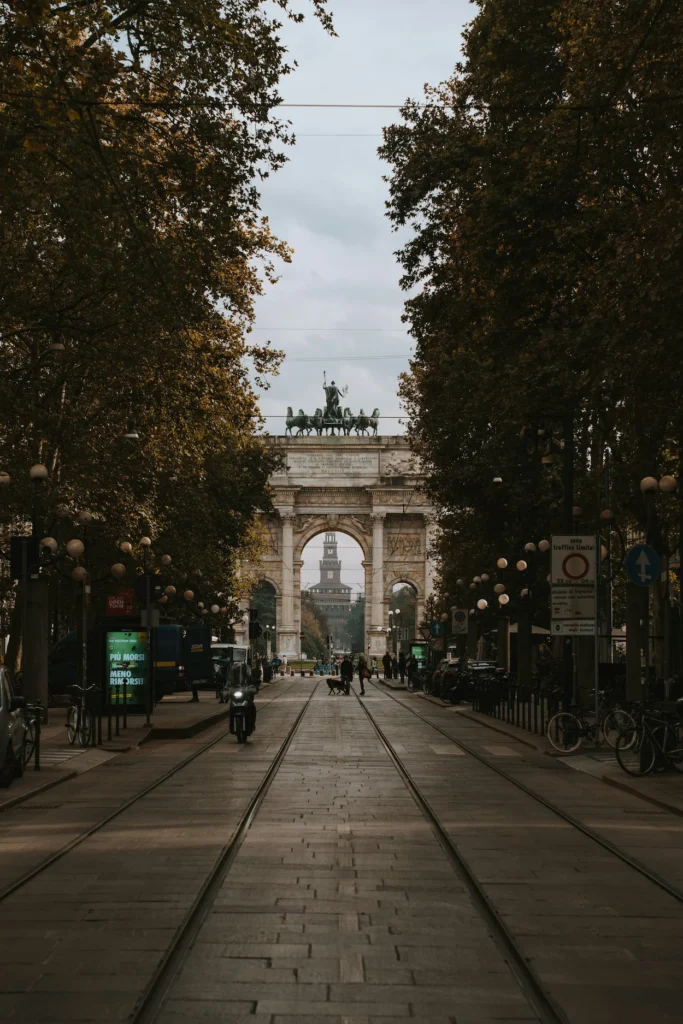 Tram tracks leading toward the historic Arco della Pace monument framed by green trees in Milan, Italy