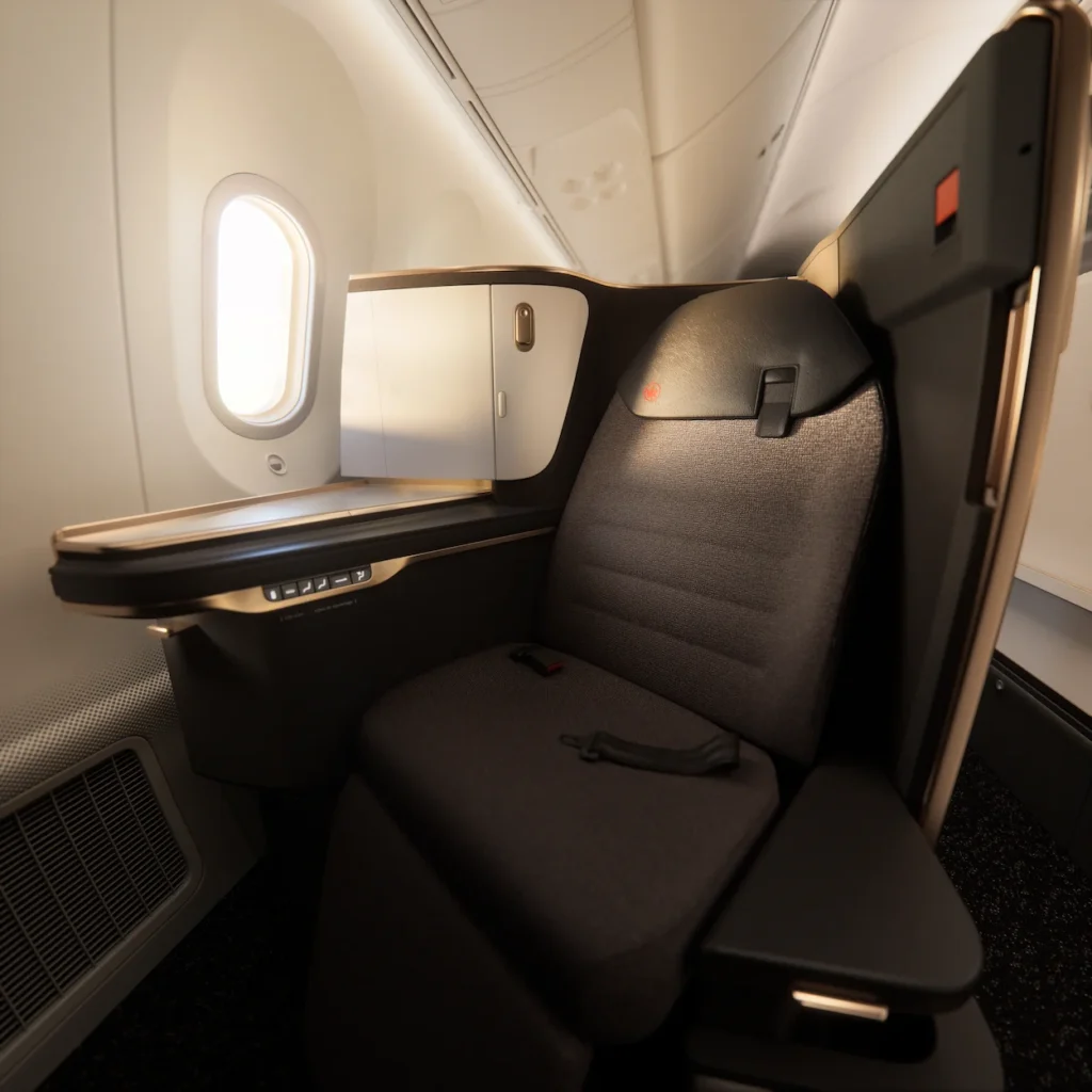 A dark gray business class pod seat next to an airplane window