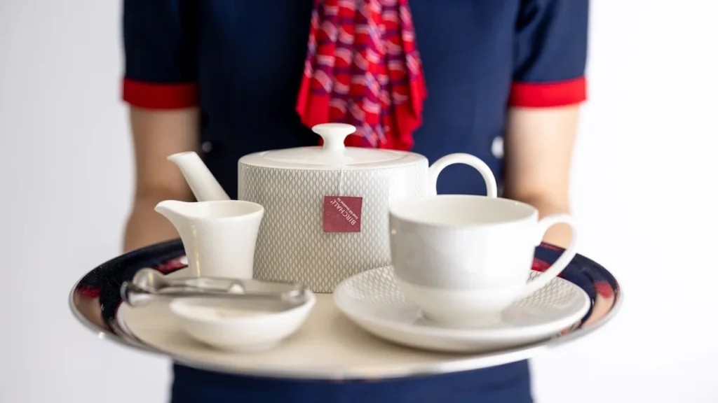 Flight attendant holding a silver tray with a porcelain teapot and teacup.