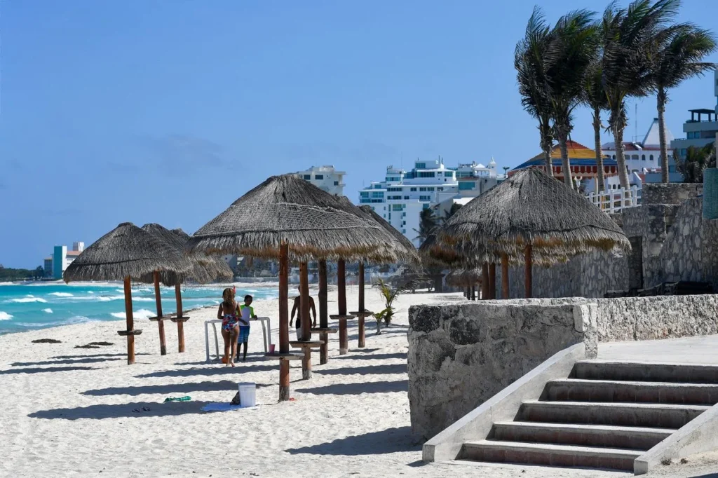 Thatch-roofed palapa umbrellas over lounge chairs on a sandy beach in Cancun, Mexico