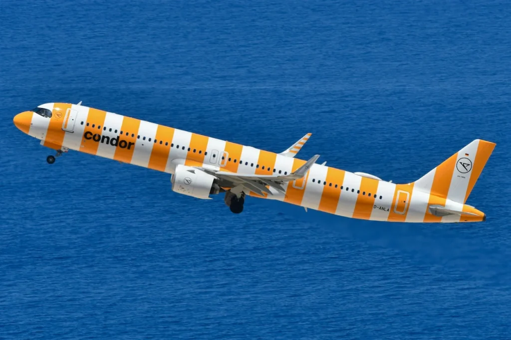 Condor Airbus A321neo airplane in orange and white vertical stripes climbing over blue ocean water