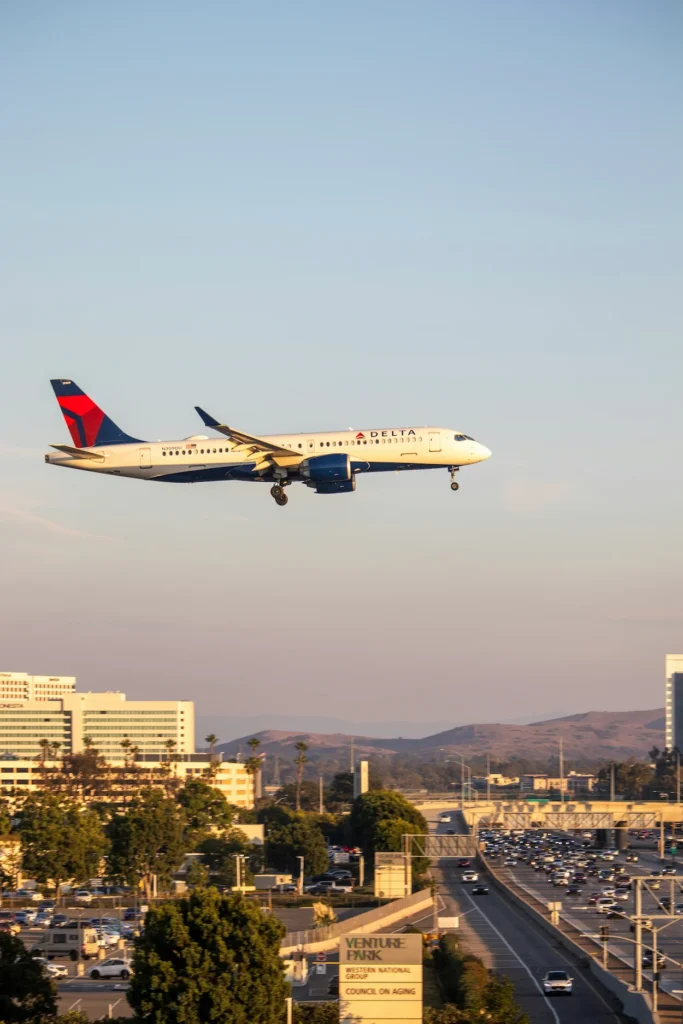 Delta Air Lines Airbus A220 passenger airplane on landing approach over city buildings and highway traffic