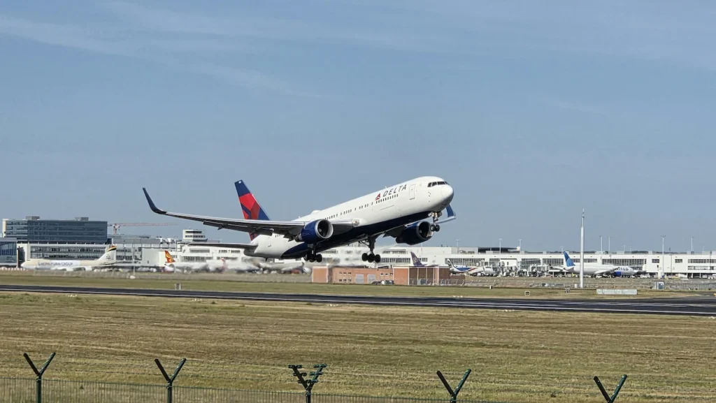 Delta Air Lines Boeing 767 widebody airplane angling upward into a pale blue sky during takeoff from an airport runway