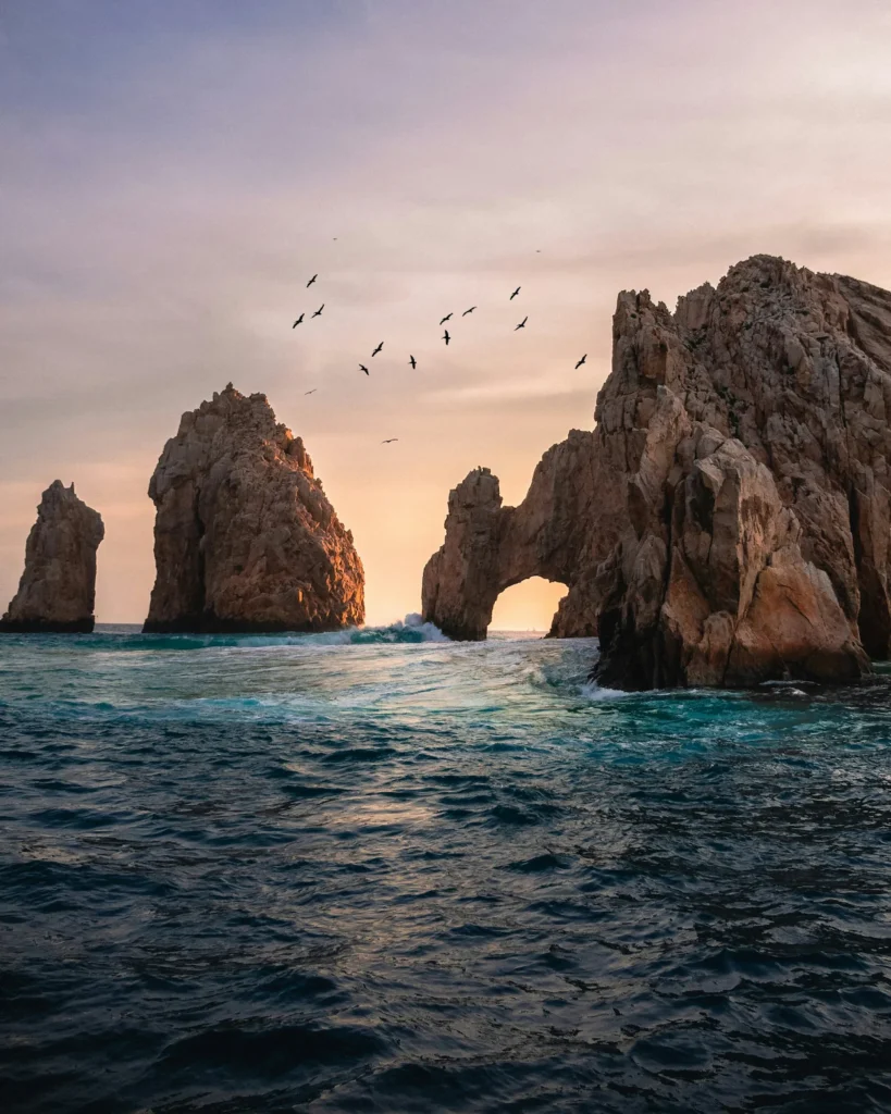 The Arch of Cabo San Lucas rock formation in Mexico with birds flying overhead at sunset