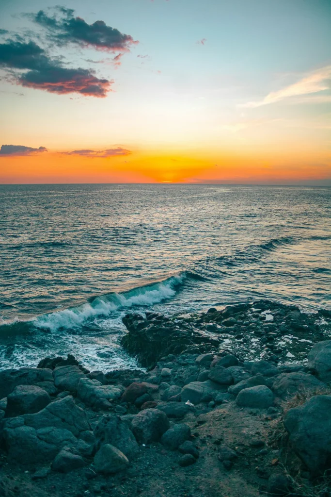 Ocean waves crashing onto rocky shores during a golden sunset at El Tunco beach