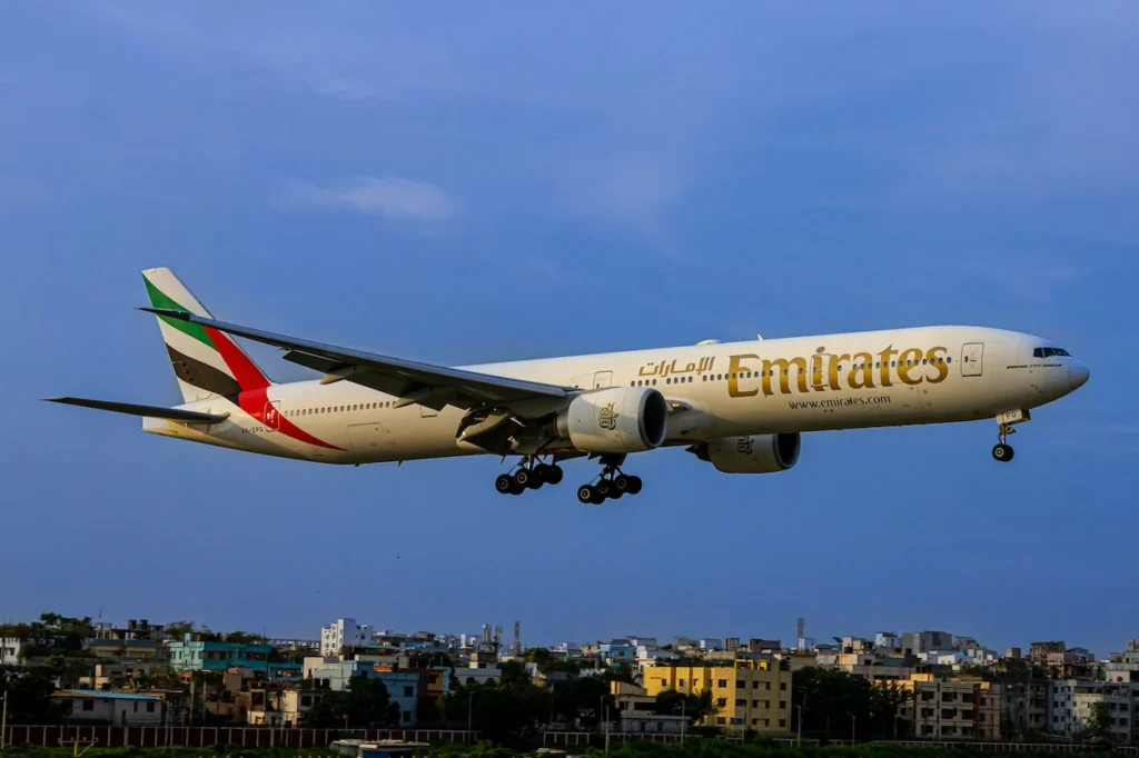 Emirates Boeing 777-300ER widebody aircraft with landing gear deployed descending over a city landscape