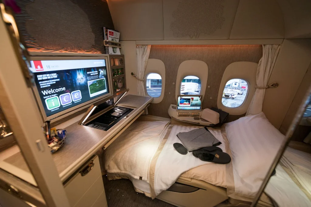 Luxury enclosed First Class suite on an airplane with a large entertainment screen and a fully flat bed