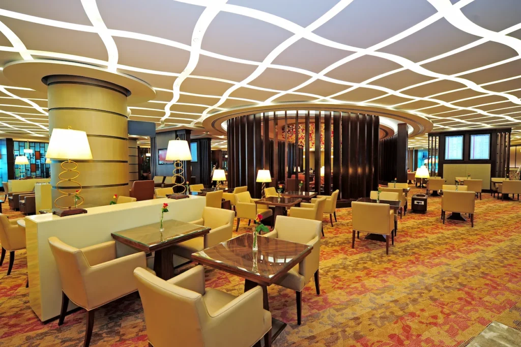 Spacious, luxury airport lounge with gold columns, glowing wavy ceiling lights, and elegant seating areas