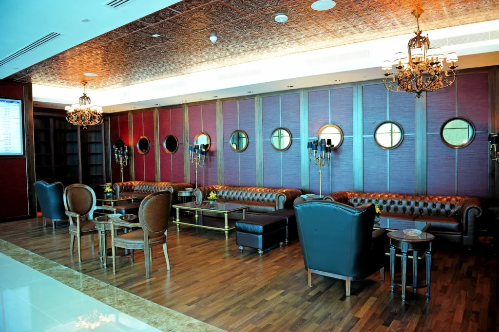 A luxury airport lounge room with leather Chesterfield sofas, a textured copper ceiling, and ornate chandeliers