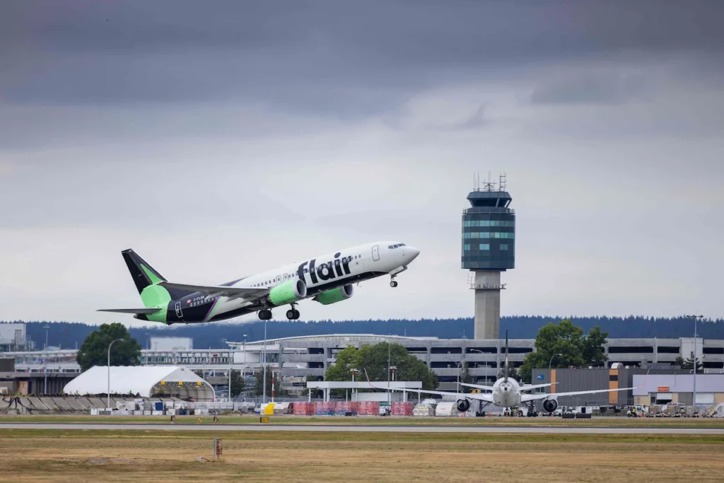 Flair Airlines Boeing 737 MAX airplane taking off past an airport control tower