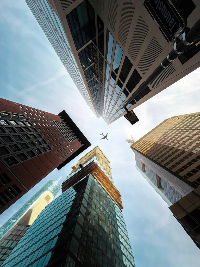 Low-angle perspective looking straight up at towering Frankfurt skyscrapers with a commercial jet flying overhead