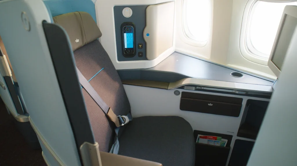 A blue and grey airplane business class pod seat next to a window