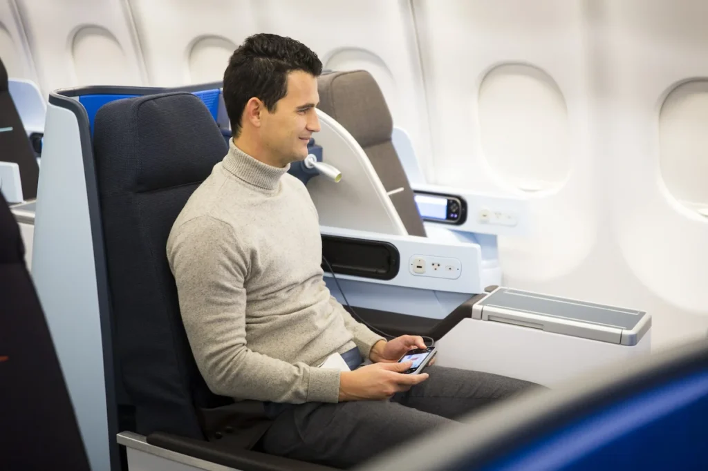 Man sitting in a blue KLM business class seat holding a remote control