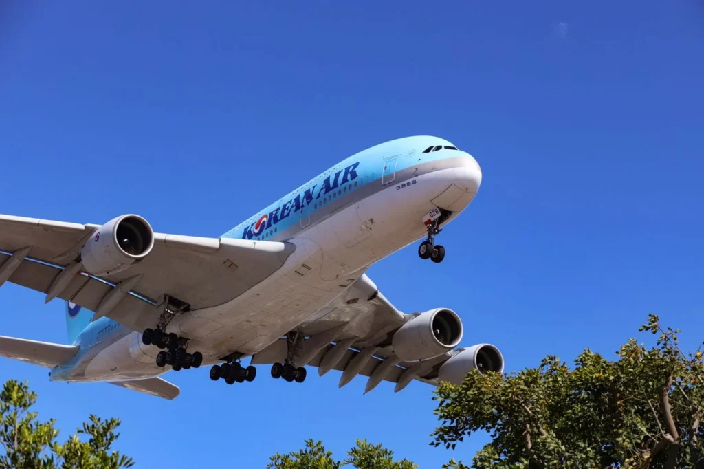 A Korean Air Airbus A380 double-decker aircraft descending over green trees