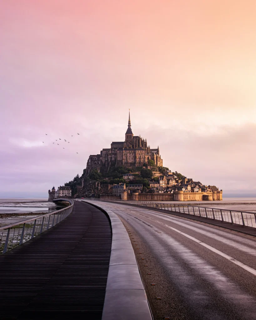 The tidal island abbey of Mont-Saint-Michel at sunset viewed from the main access bridge