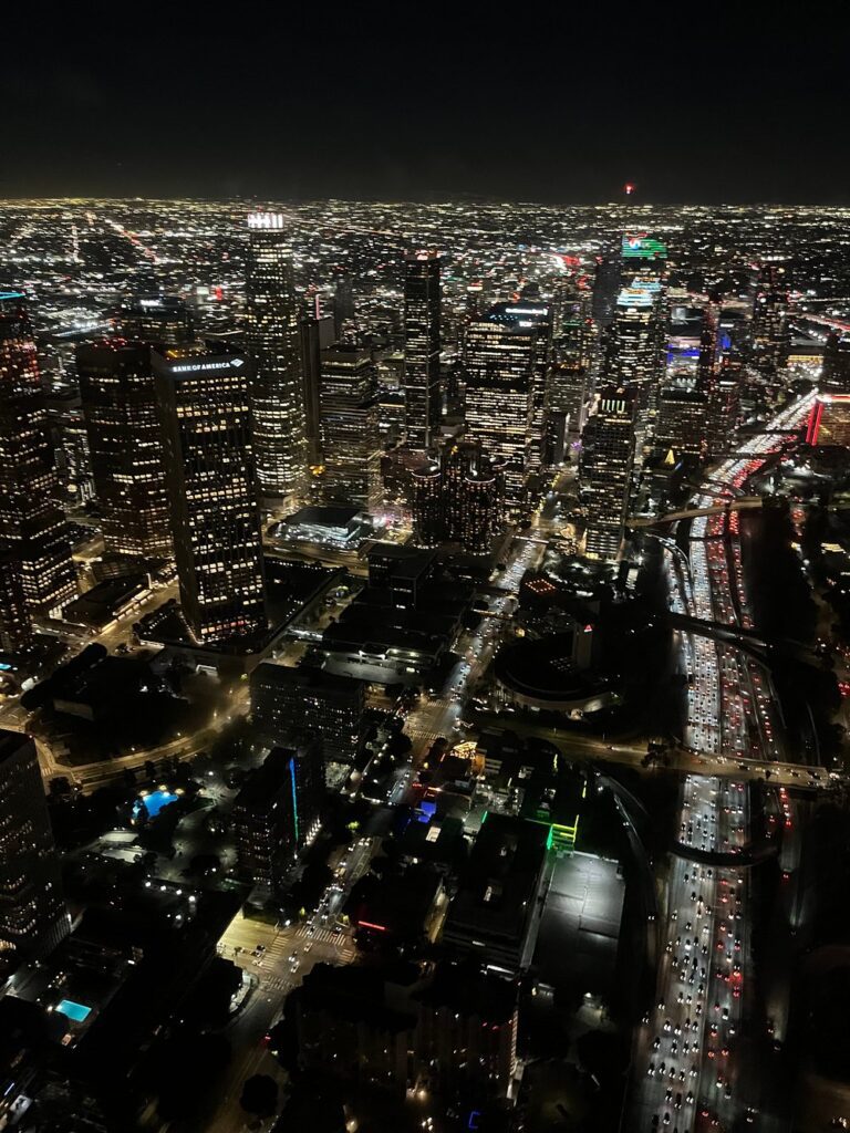 A nighttime aerial view of downtown Los Angeles during a Hollywood helicopter tour, with city lights stretching into the distance.