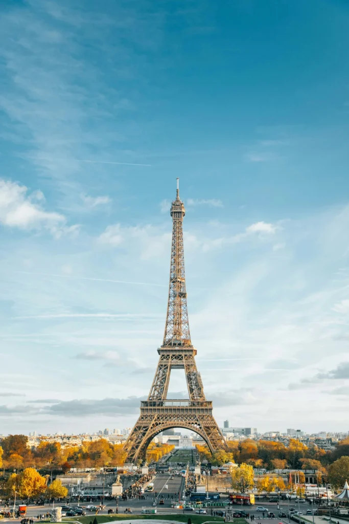The Eiffel Tower towering over autumn trees in Paris under a bright blue sky