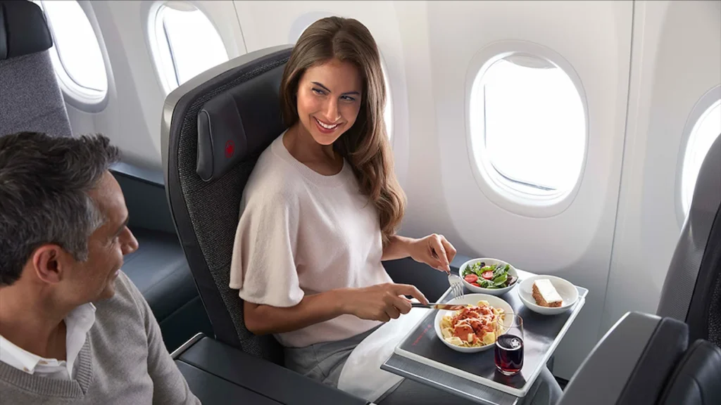 A woman eating a meal on a tray table in a premium airplane seat