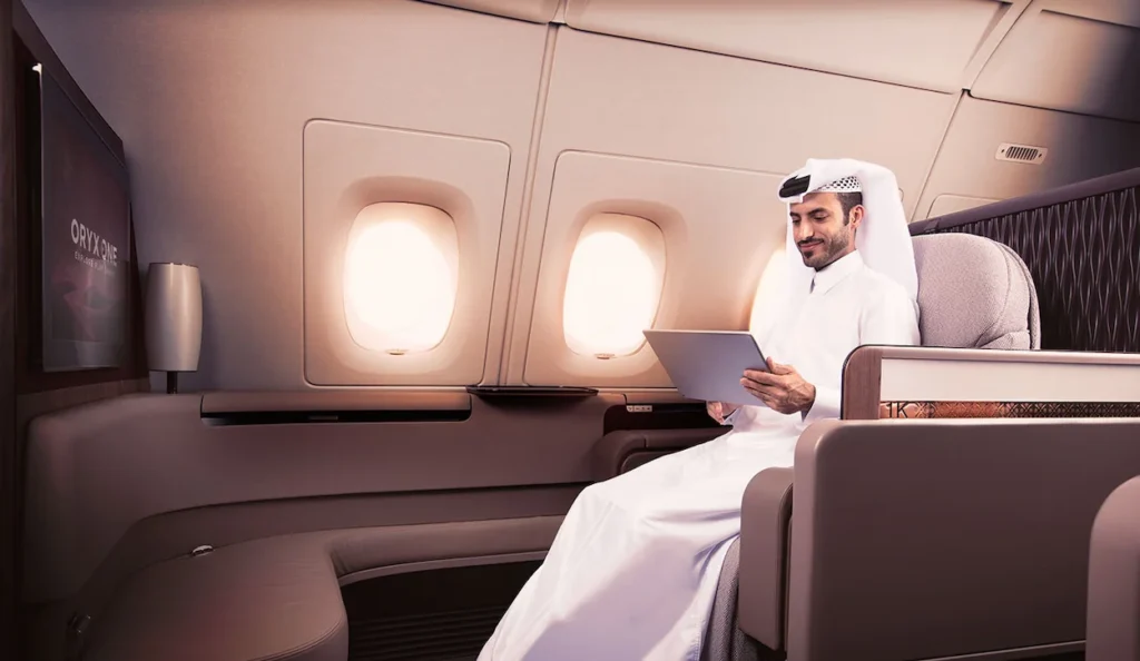 A man in traditional Qatari attire using a tablet inside a Qatar Airways A380 First Class suite