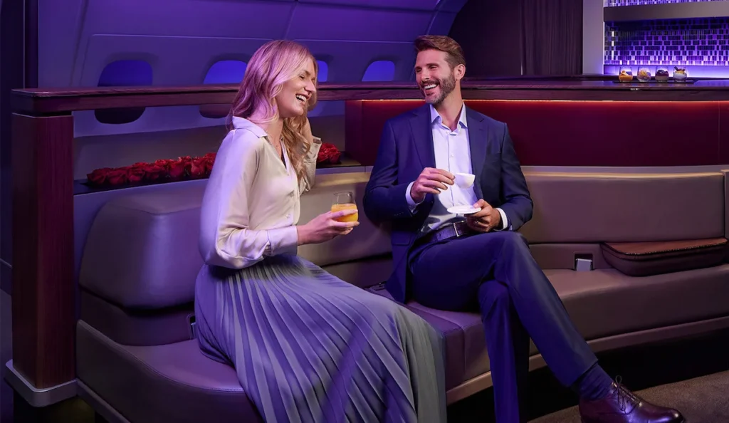 A smiling man and woman chatting on a curved leather sofa inside the Qatar Airways A380 onboard lounge
