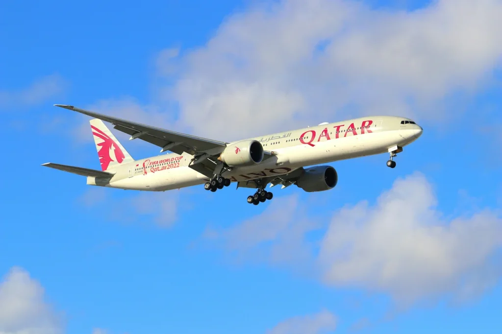 A Qatar Airways Boeing 777-300ER in FIFA World Cup 2022 livery landing against a blue sky