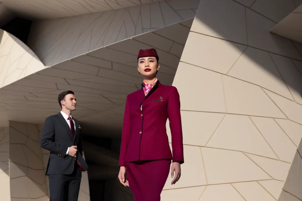 A male and female Qatar Airways flight attendant posing in uniform against a geometric architectural background