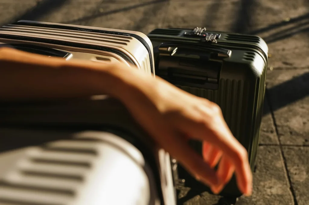 Two Rimowa suitcases on the ground with a person's hand resting on top