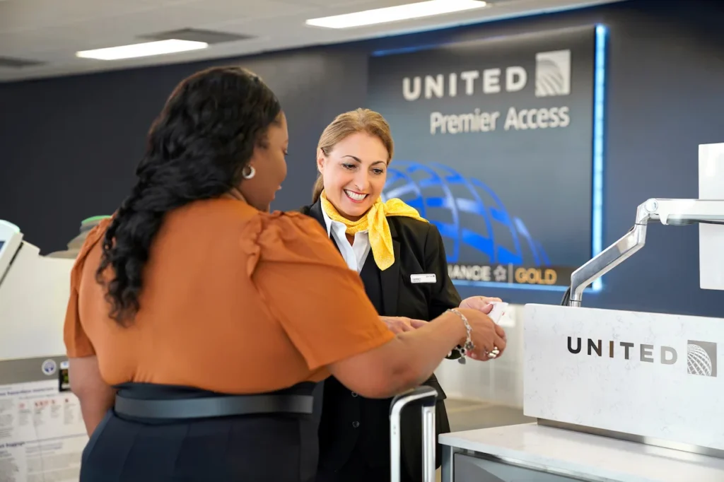 A ticket agent smiles while assisting a passenger at a United Premier Access check-in desk