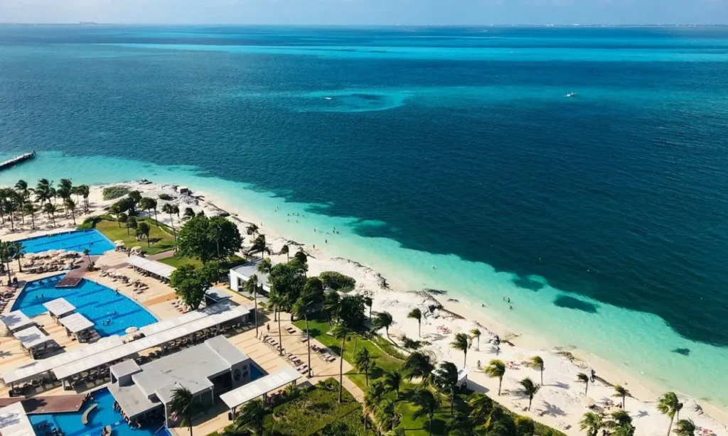 Aerial view of Cancun’s white sandy beach and turquoise ocean next to a resort pool area.