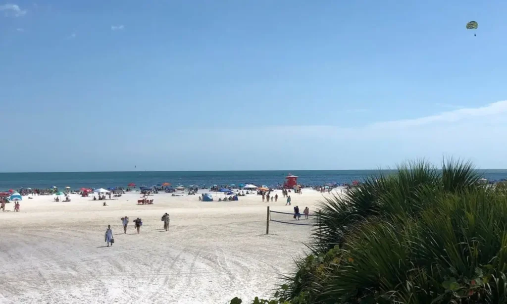 A sunny day at Siesta Beach with people, umbrellas, and a clear blue sky.