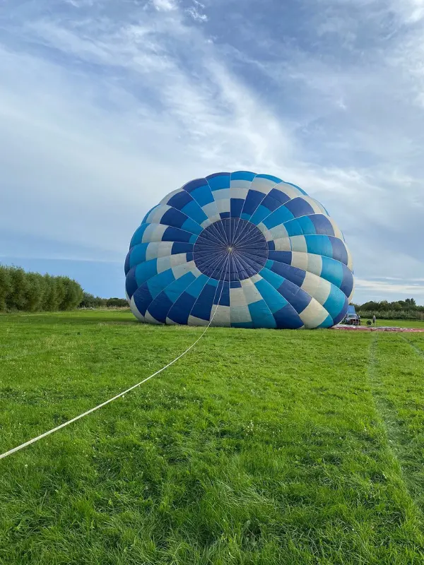 Blue and white hot air balloon being inflated on a grassy field at Fly Away Ballooning.