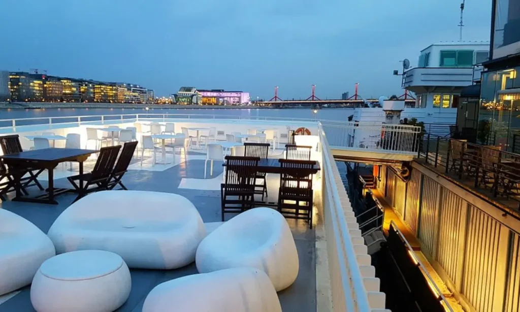 Modern outdoor seating on the deck of A38 with a river view at dusk.