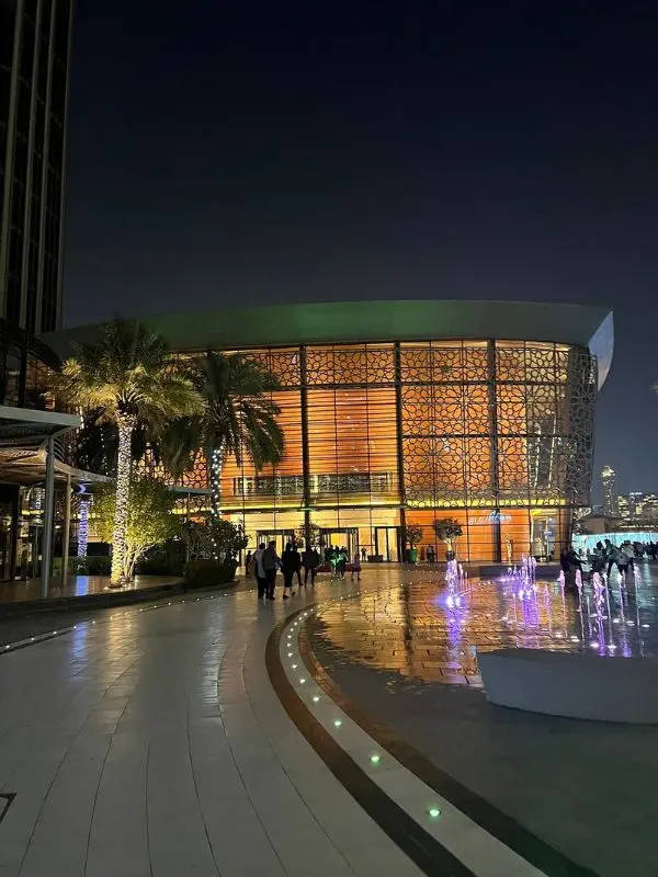 The exterior of Dubai Opera at night with glowing orange lights and a reflective walkway.