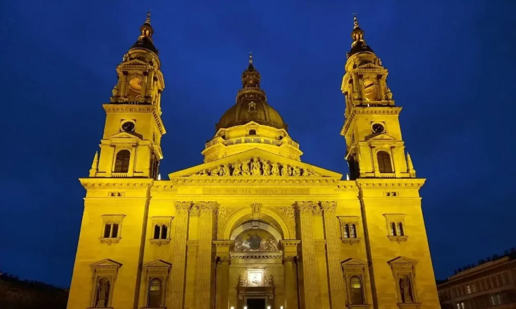 The grand illuminated facade of St. Stephen’s Basilica against a deep blue sky.