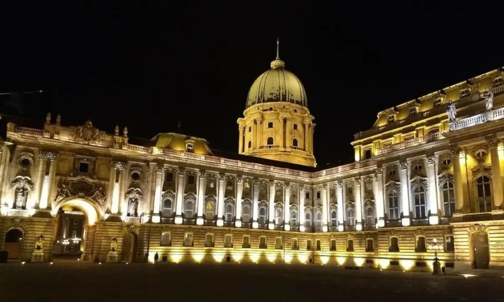 Buda Castle illuminated at night with its grand dome and ornate facade.