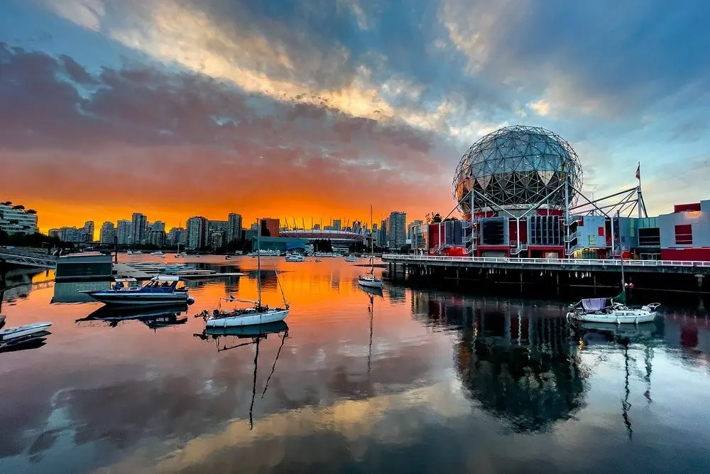 Boats on the water in front of the dome-shaped Science World at sunset.