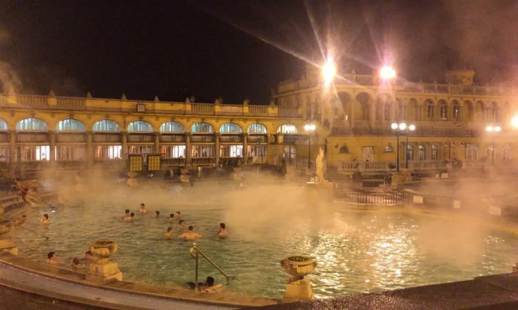 People relaxing in the steaming outdoor pools of Széchenyi Baths at night.