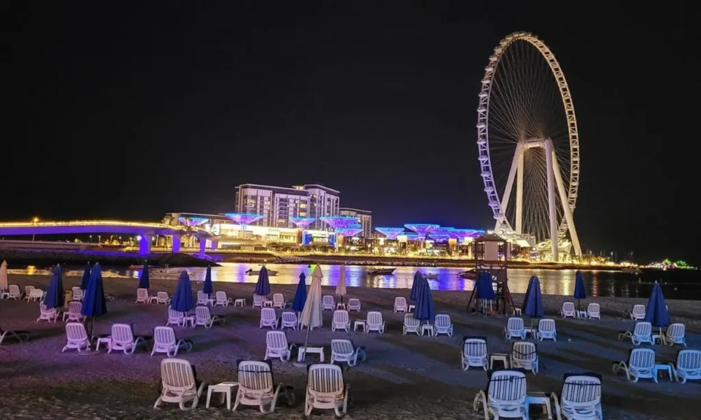 The Walk at JBR at night with beach chairs, umbrellas, and a large Ferris wheel in the background.