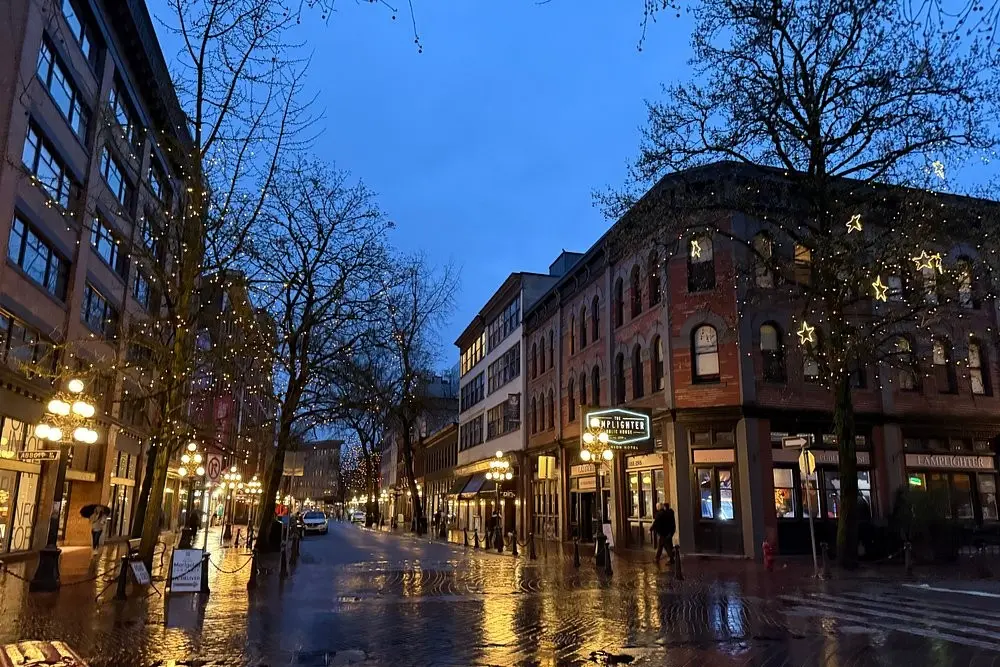 Evening street view of Gastown with old buildings and string lights.