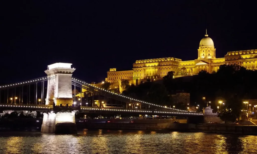 A nighttime Danube cruise view with the Chain Bridge and Buda Castle lit up.